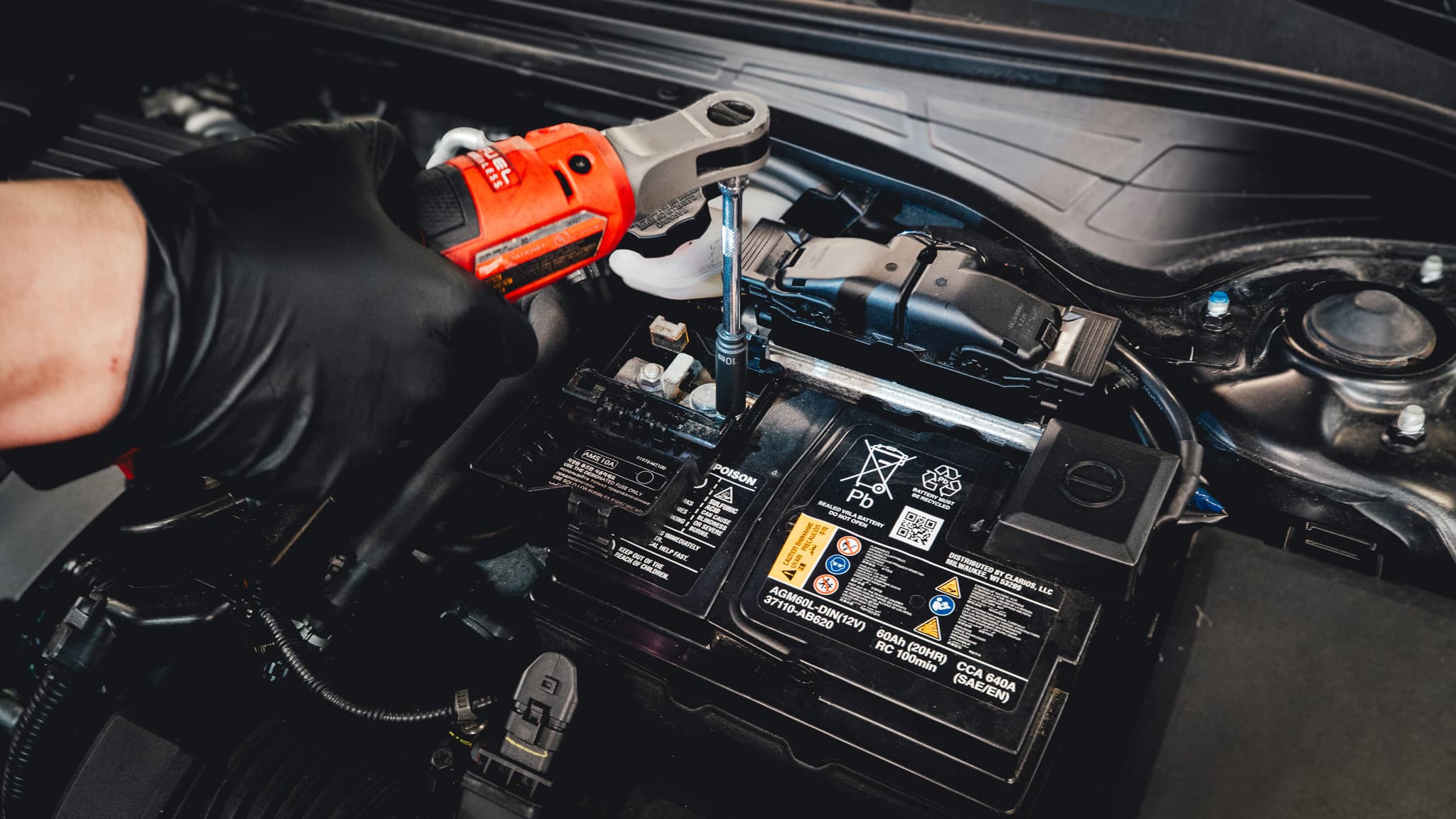 Technician using a power tool while working near a vehicle battery.